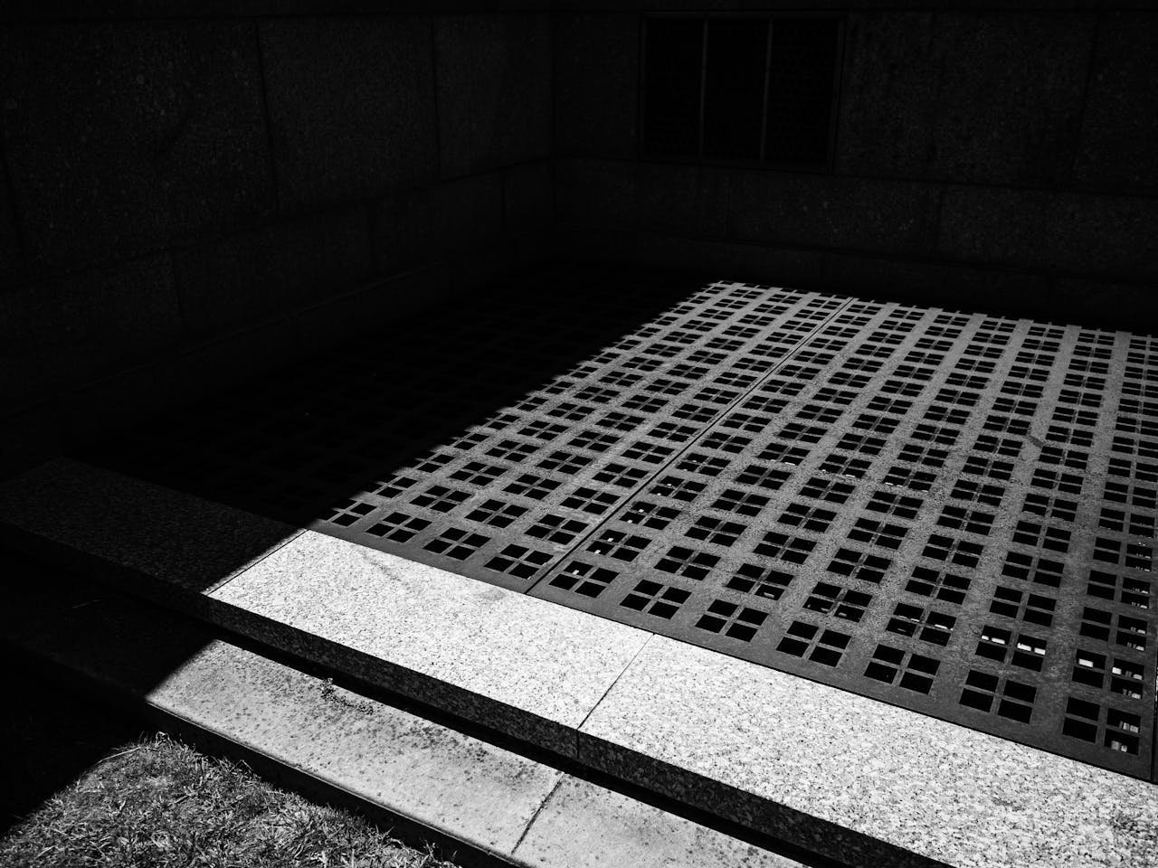 Minimalist black and white photo of architectural walls and shadows on a grill.