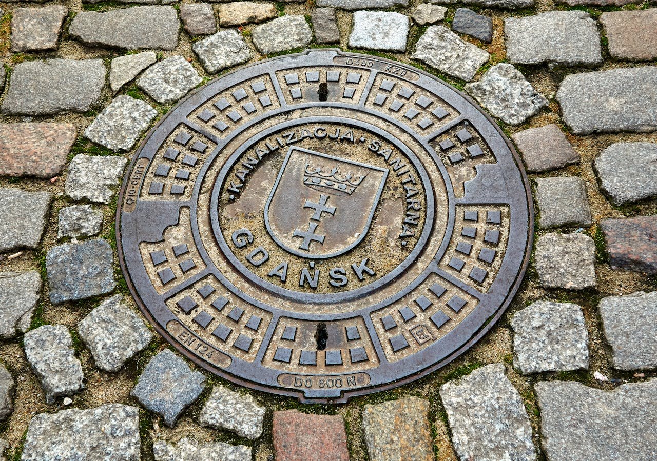 Circular Gdańsk manhole cover set in cobblestone street, showcasing urban infrastructure.
