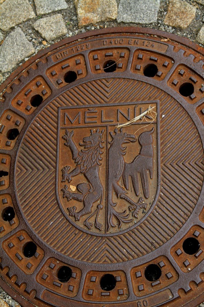 Detailed image of a Mělník manhole cover with a coat of arms design, surrounded by cobblestones.