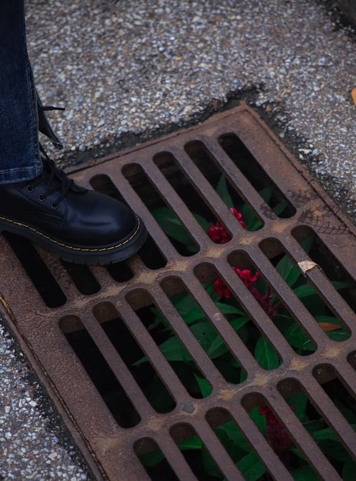 our-experience Close-up of a foot in black boot next to vibrant red flowers through a drain.