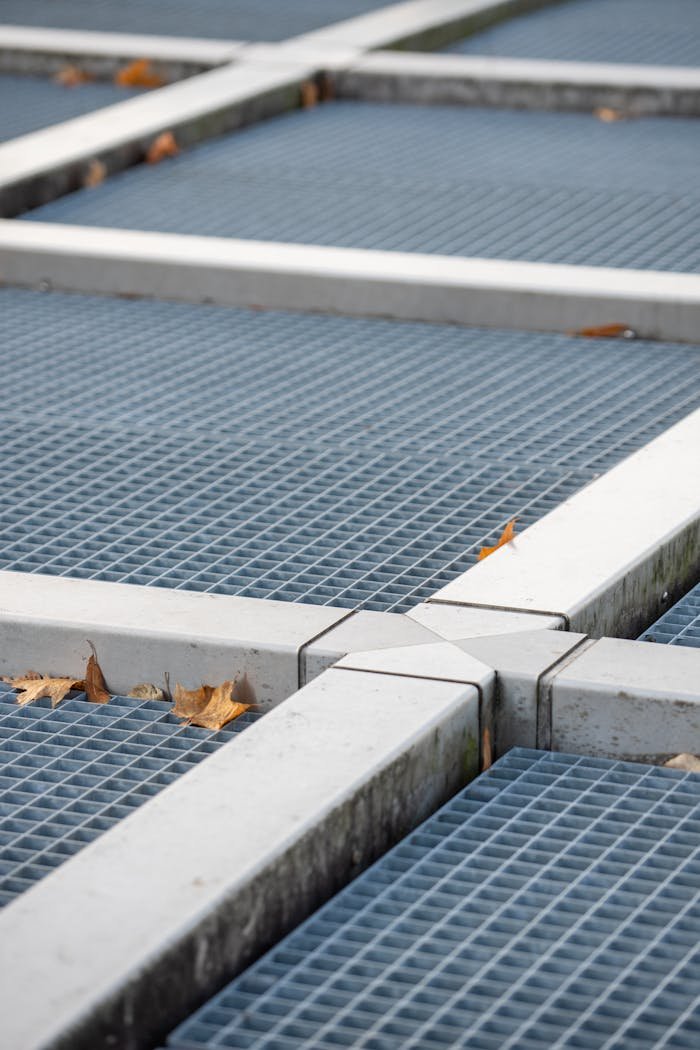 A close-up of a metal grid intersected by white beams with autumn leaves scattered on the surface.