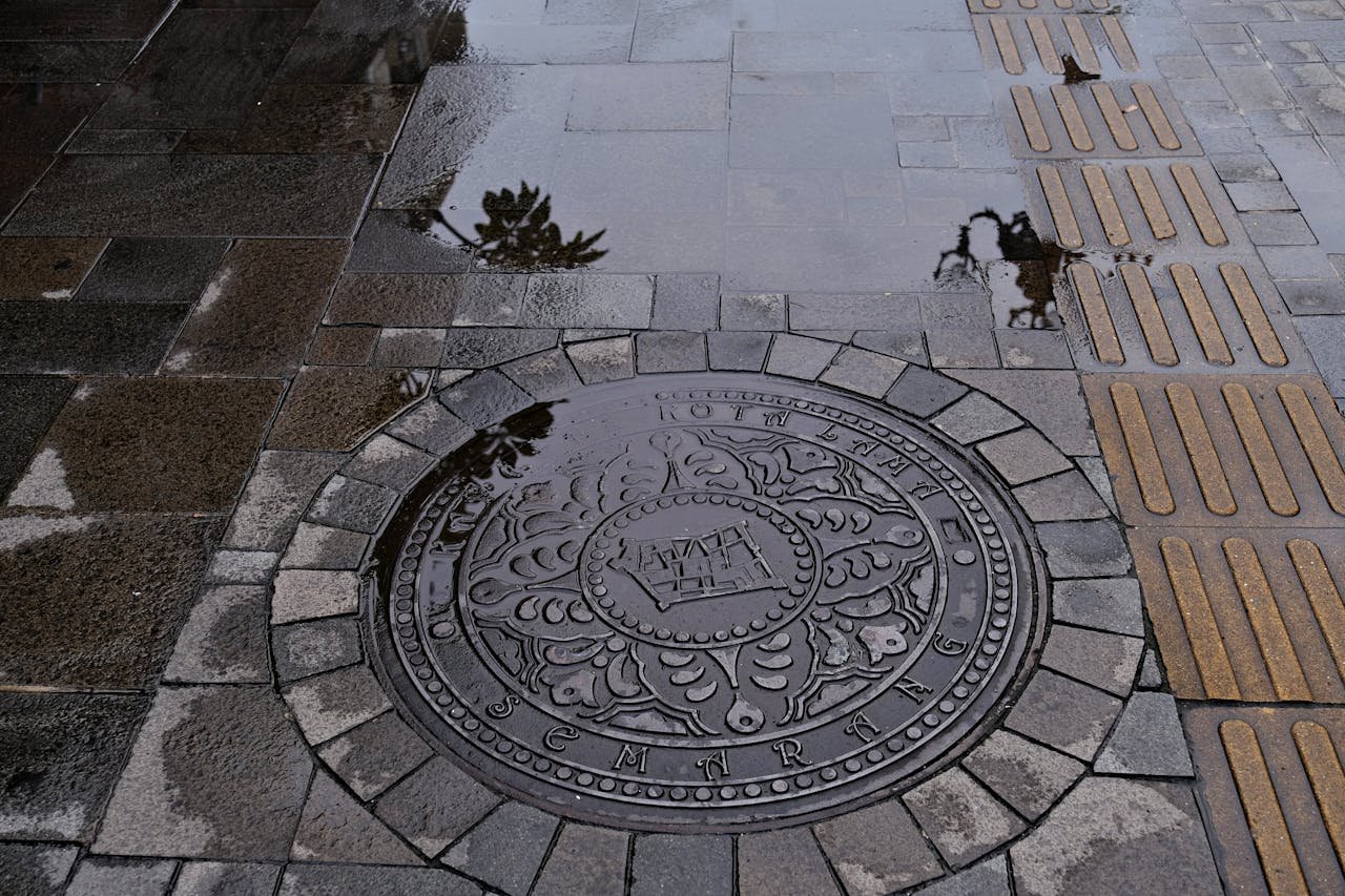 An artistic view of a decorated manhole cover in Semarang, featuring wet pavement reflections.